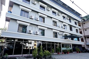 Un edificio de varios pisos con grandes ventanales, unidades de aire acondicionado y plantas en macetas en la zona de entrada.