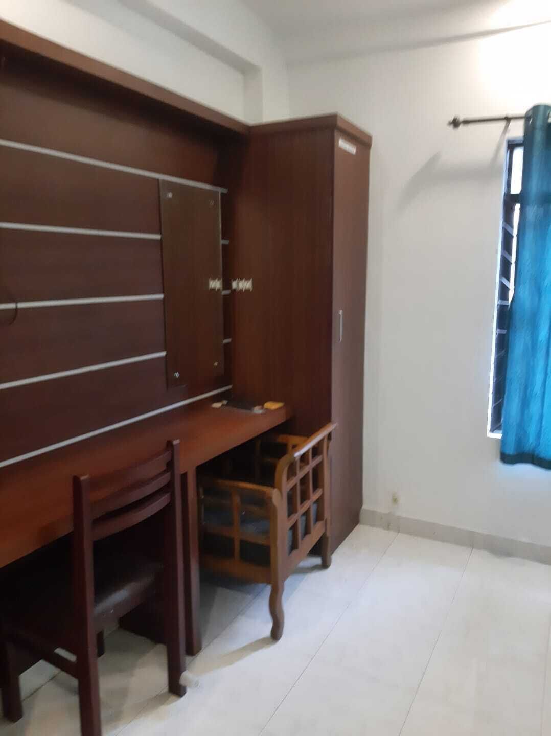 A room with a wooden desk, a chair, a wardrobe, and a window with a blue curtain.