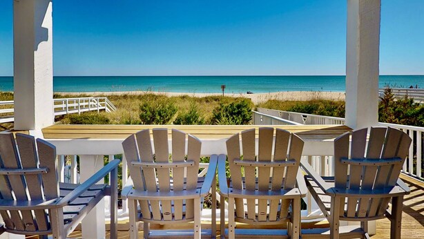 Un espace extérieur abrité, aménagé avec trois fauteuils Adirondack donnant sur une plage.