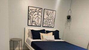 Ein Schlafzimmer mit einem Bett, einem kleinen Nachttisch, einem Sessel und zwei Wandbildern.