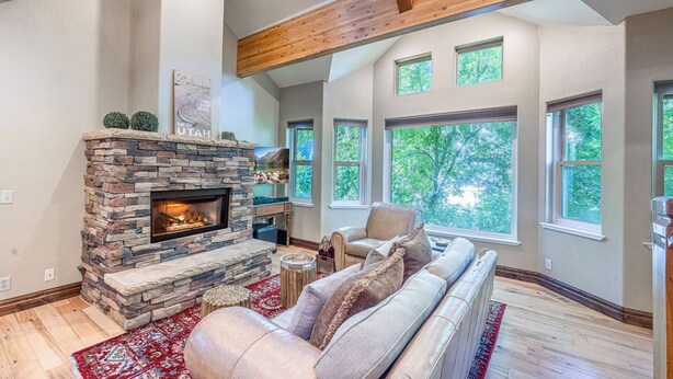 A spacious living room with a stone fireplace, large windows, and a high ceiling with exposed wooden beams. - Old Town Park City Vacation Home with Private Hot Tub, Walk to Main St or Skiing (Park City)
