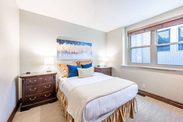 A bedroom with a bed, nightstands, a painting, and a window.