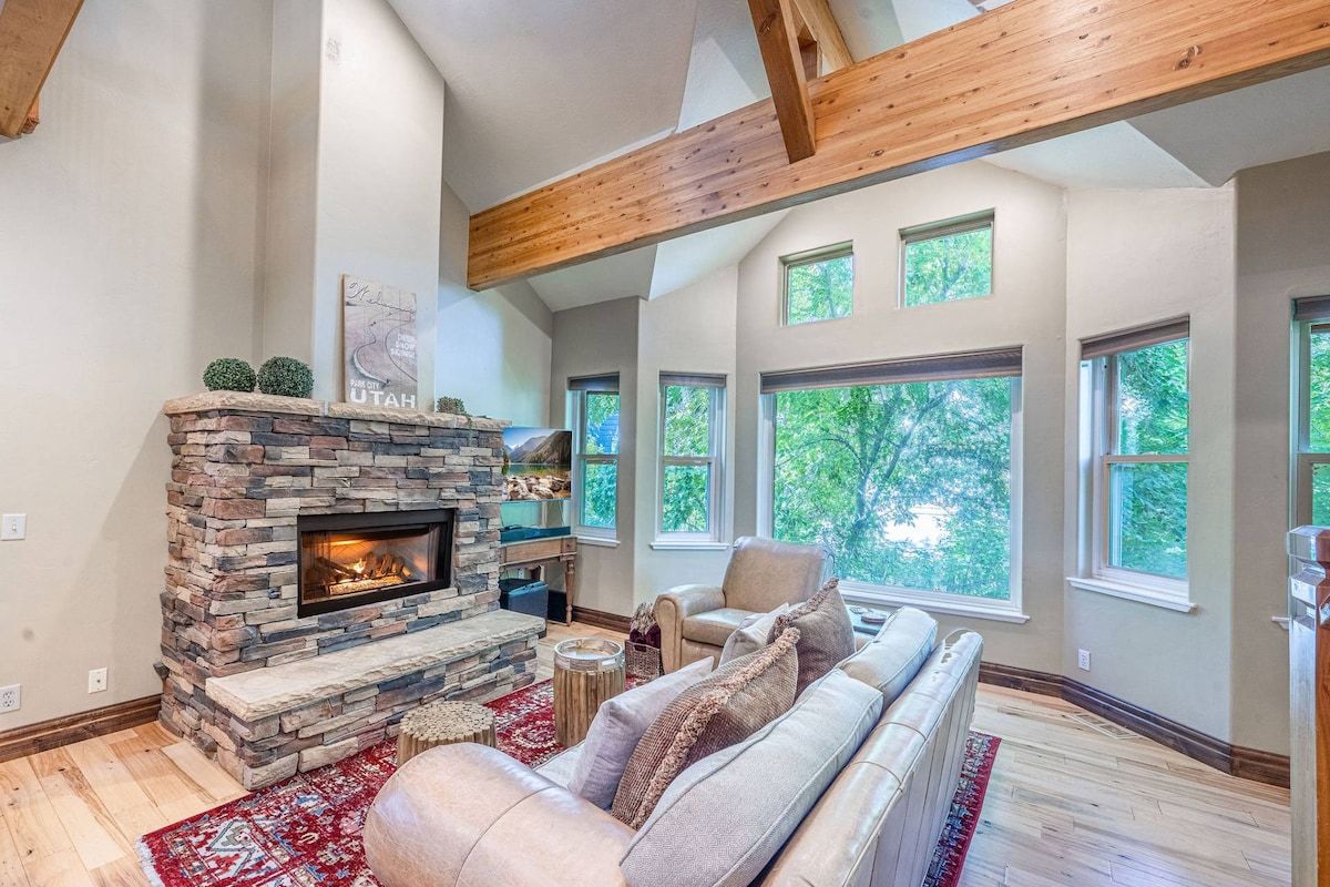 A living room with a stone fireplace, a leather sofa, and large windows.