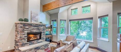 A living room with a stone fireplace, a leather sofa, and large windows.