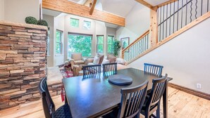 A spacious dining area with a dark wooden table and chairs, a stone accent wall, and a staircase with wooden railings. - Old Town Park City Vacation Home with Private Hot Tub, Walk to Main St or Skiing (Park City)