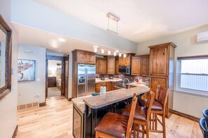 A kitchen with wooden cabinets, a central island with bar stools, and a view of the adjacent living area.