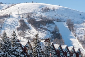 A snow-covered ski slope with a ski lift, surrounded by buildings with red roofs and snow-covered trees.