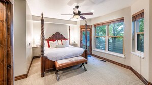 A four-poster bed with a wooden headboard and footboard, a ceiling fan, and a large window with a view of trees. - Old Town Park City Vacation Home with Private Hot Tub, Walk to Main St or Skiing (Park City)