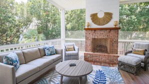 A covered patio with a brick fireplace, a sofa, a round table, and two chairs. - Upscale, Custom Home 3 Doors From Beach w/ Private Pool, Hot Tub & Screened Porch, Bunk Room & Den (Isle of Palms)