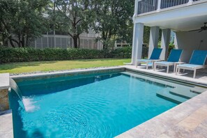 A swimming pool with clear blue water, surrounded by a white pool deck and blue lounge chairs.