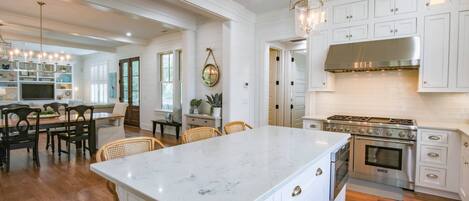 A spacious kitchen with white cabinetry, a large island, and a stainless steel range hood.