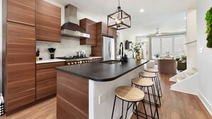 A modern kitchen with wooden cabinets, a central island with stools, and a hanging light fixture.