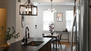 A modern kitchen with a central island, a dining area with a table and chairs, and a chandelier.
