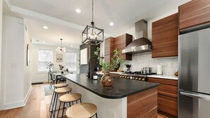 A modern kitchen with a central island, bar stools, stainless steel appliances, and wooden cabinetry.