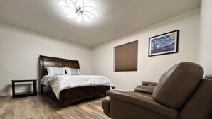 Een slaapkamer met een bed, een massagestoel, een nachtkastje, een plafondventilator en een schilderij aan de muur.