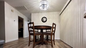 Een eetgedeelte met een houten tafel en stoelen, een klok aan de muur en een plafondlamp.