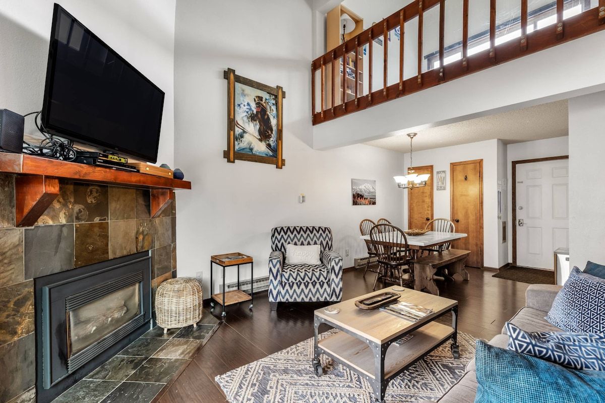 Ein Wohnzimmer mit Kamin, Fernseher, Essbereich und Treppe.