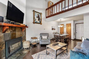 Un salon avec une cheminée, un téléviseur, un coin repas et un escalier.