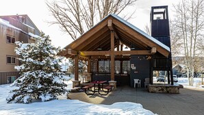 Ein hölzernes Pavillon mit Bänken und einem Kamin aus Stein, umgeben von Schnee.