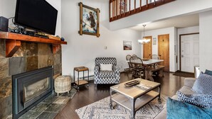 Ein geräumiger Wohnbereich mit Kamin, Fernseher, Esstisch und Stühlen sowie einer Treppe.