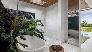Un baño moderno con una amplia bañera independiente, una pared de piedra y vistas a una piscina.