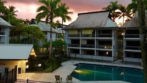 A hotel with multiple floors, a swimming pool, and palm trees.