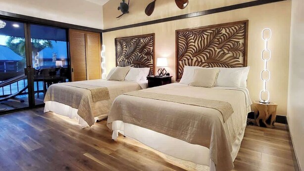 A hotel room with two beds, a wooden floor, a balcony with a view, and decorative wall art.