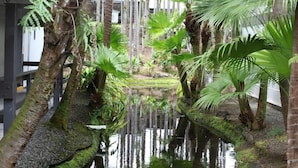A serene indoor garden with a water feature, surrounded by tall palm trees and ferns.