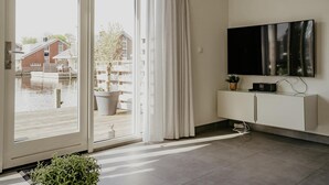 A modern living room with a sliding glass door leading to a balcony, a flat-screen TV mounted on the wall, and a minimalist white cabinet. - luxury apartment with waterside terrace (Uitgeest)