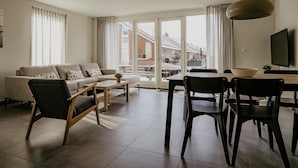 A modern living room with a sofa, chairs, a dining table, and a TV. - luxury apartment with waterside terrace (Uitgeest)