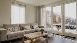 A modern living room with a sofa, a wooden coffee table, and a view of a dock area. - luxury apartment with waterside terrace (Uitgeest)
