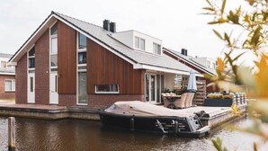 A house with a dock extending into a canal, a covered boat, and a patio with outdoor furniture. - luxury apartment with waterside terrace (Uitgeest)