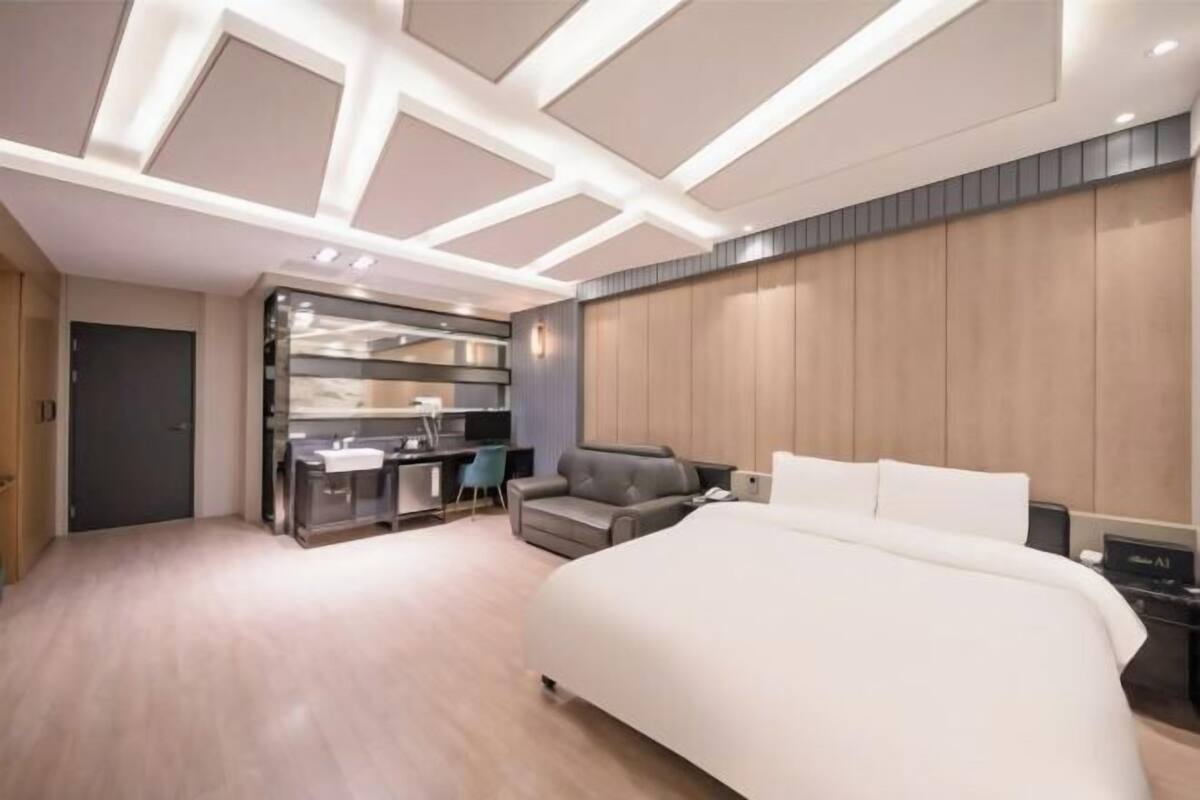 A modern hotel room with a large bed, a desk with a chair, and a kitchenette area.