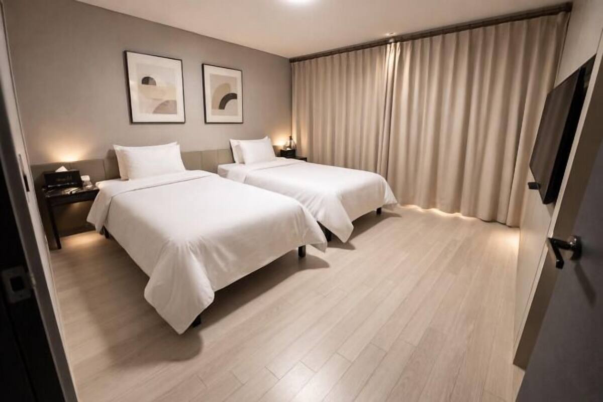 A hotel room with two beds, a flat-screen TV, and a large window with curtains.