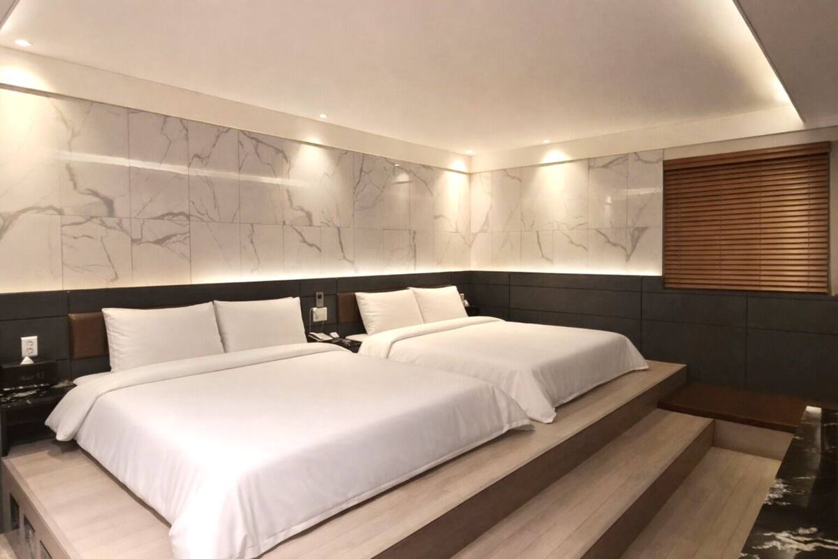 A modern hotel room with a large bed, a bedside table, and a built-in bench.