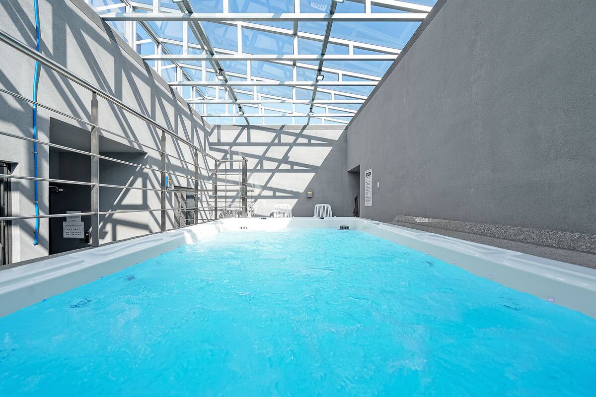 An indoor swimming pool with a glass ceiling, metal beams, and a grey wall.