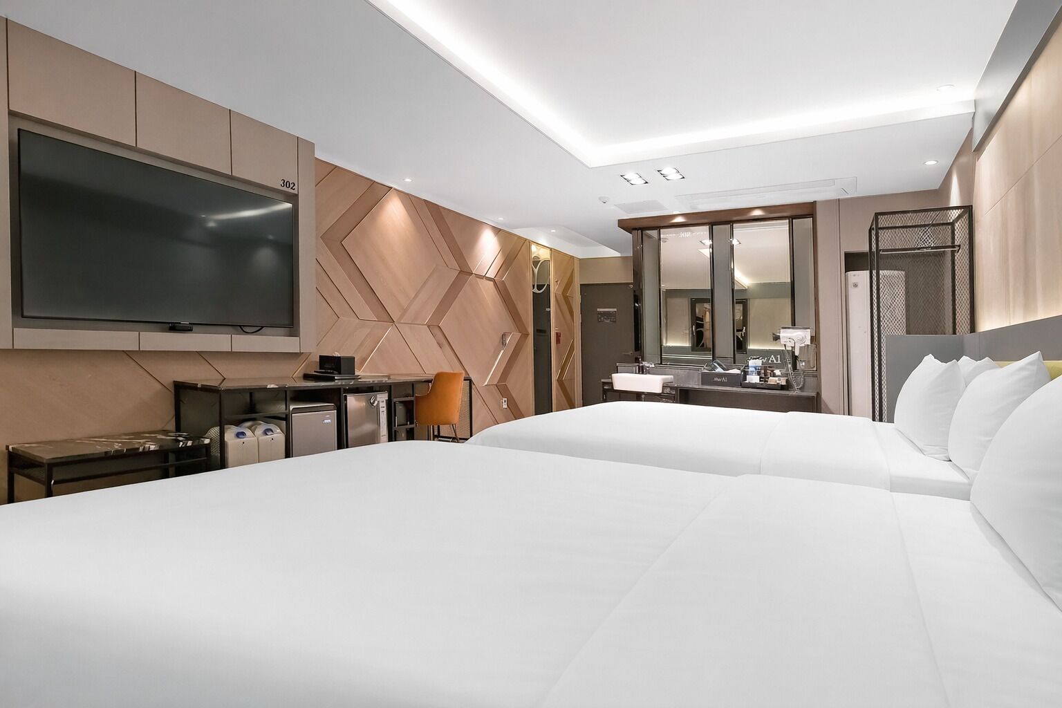 A hotel room with a large bed, a desk with a computer, a TV, a mirror, and a minibar.
