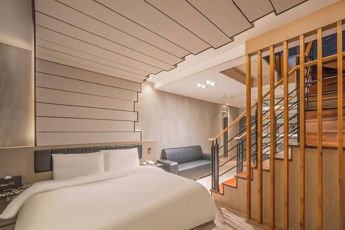 A modern hotel room with a large bed, a seating area, and a staircase.