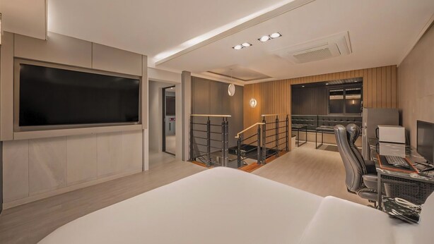 A modern hotel room with a large bed, a desk with a computer, a TV, and a staircase leading to a dining area. - Pohang A1Hotel Haedo (Pohang)
