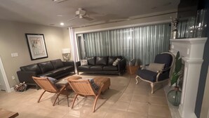Een woonkamer met een zwarte bank, twee rieten fauteuils, een salontafel en een open haard.
