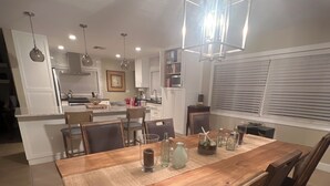 Een ruime eethoek met een houten tafel en stoelen, een hanglamp en een keuken op de achtergrond.