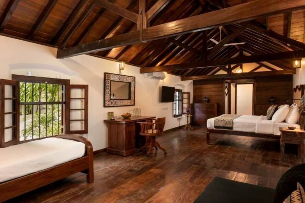 A rustic room with a wooden ceiling, a bed, a desk, and a sofa.