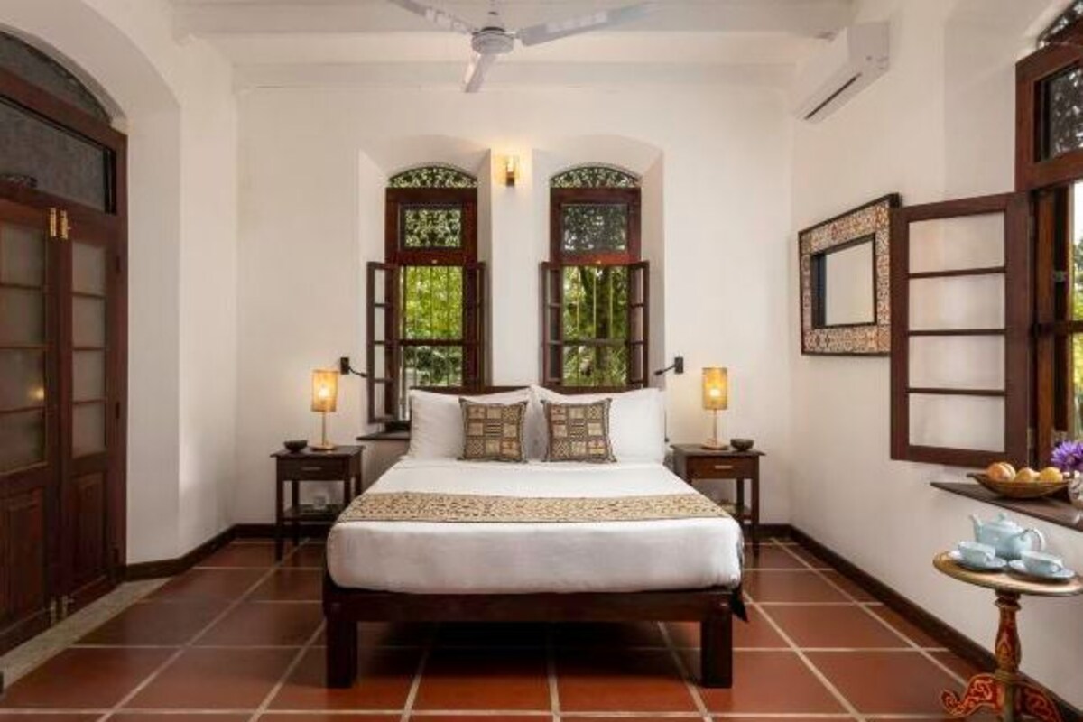 A bedroom with a large bed, two nightstands, a ceiling fan, and a window with a view of greenery.