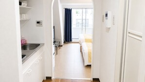 Un couloir étroit mène à une chambre à coucher qui contient un lit, un téléviseur et une fenêtre avec des rideaux.