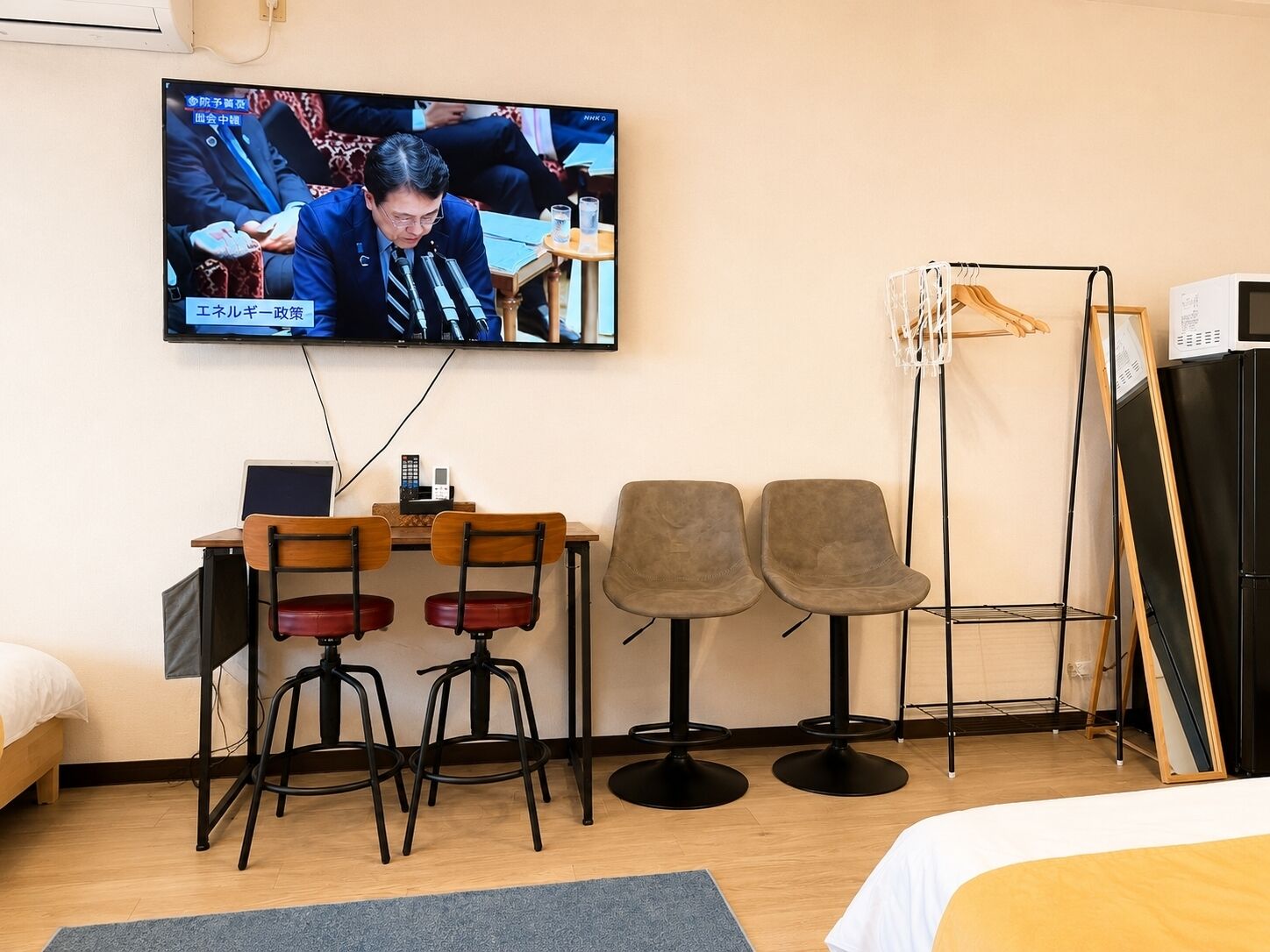 Habitación de hotel con televisor, escritorio con sillas, cama y perchero.