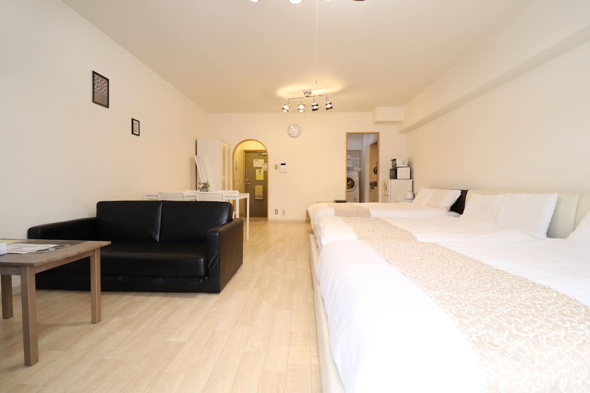 Habitación de hotel con cama, sofá, una mesa y una lavadora al fondo.