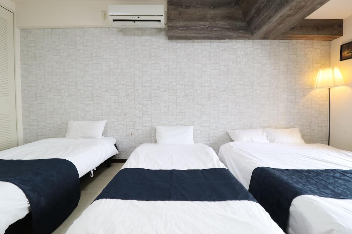 Habitación de hotel con tres camas, pared con diseño de ladrillo, techo con vigas a la vista y aire acondicionado de pared.