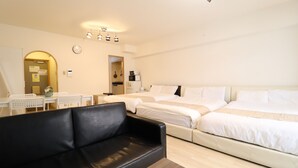 Une chambre d’hôtel dotée d’un grand lit, d’un canapé en cuir noir, d’un coin repas avec une table et des chaises, et d’un coin cuisine avec un réfrigérateur et une horloge murale.