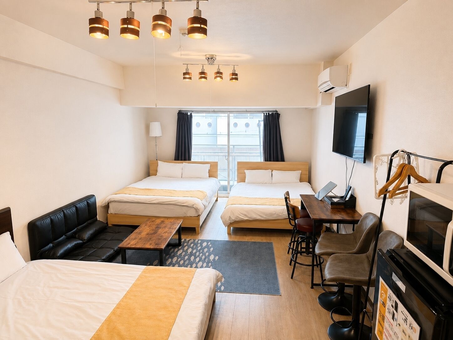 A hotel room with two beds, a sofa, a desk, a TV, and an air conditioning unit.