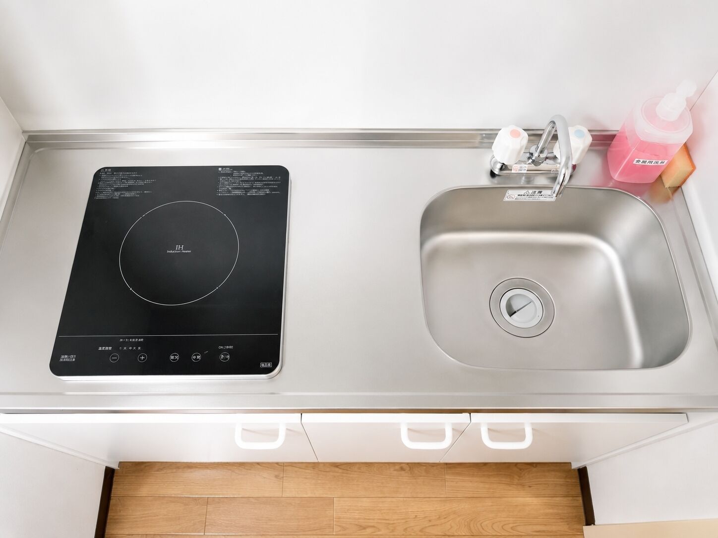 A kitchen with a built-in induction cooktop, a stainless steel sink, and a small bottle of dish soap.